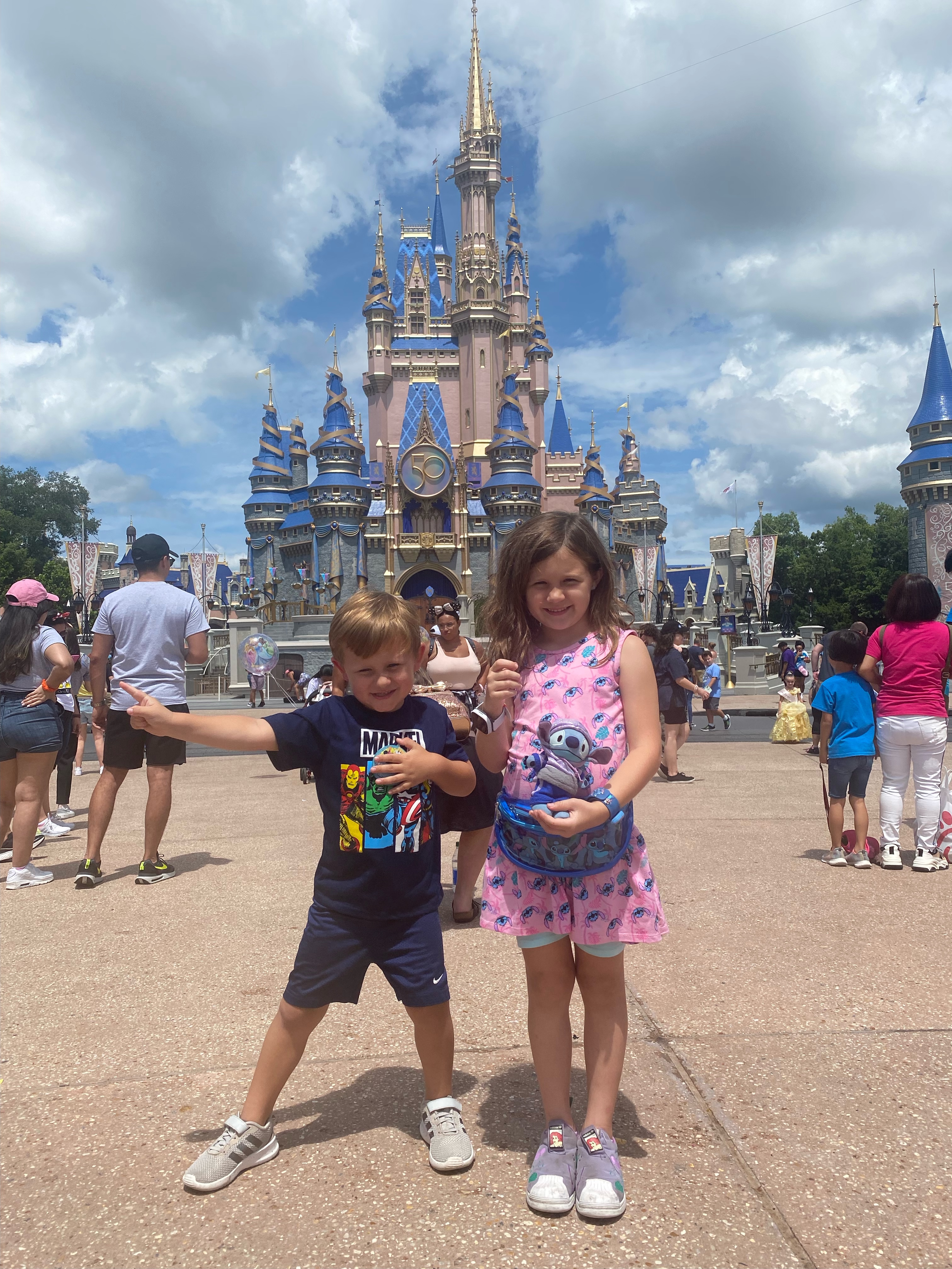 A young boy and girl pose in front of Cinderella's Castle at Disney World, while others mill around them.